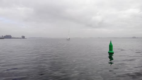 Navigationsbojen-Dümpeln-Auf-Einem-Ruhigen-See,-Während-Ein-Segelschiff-Näher-Kommt