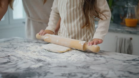 manos de niño rodando la masa en casa de cerca. familia desconocida cocinando pastel juntos