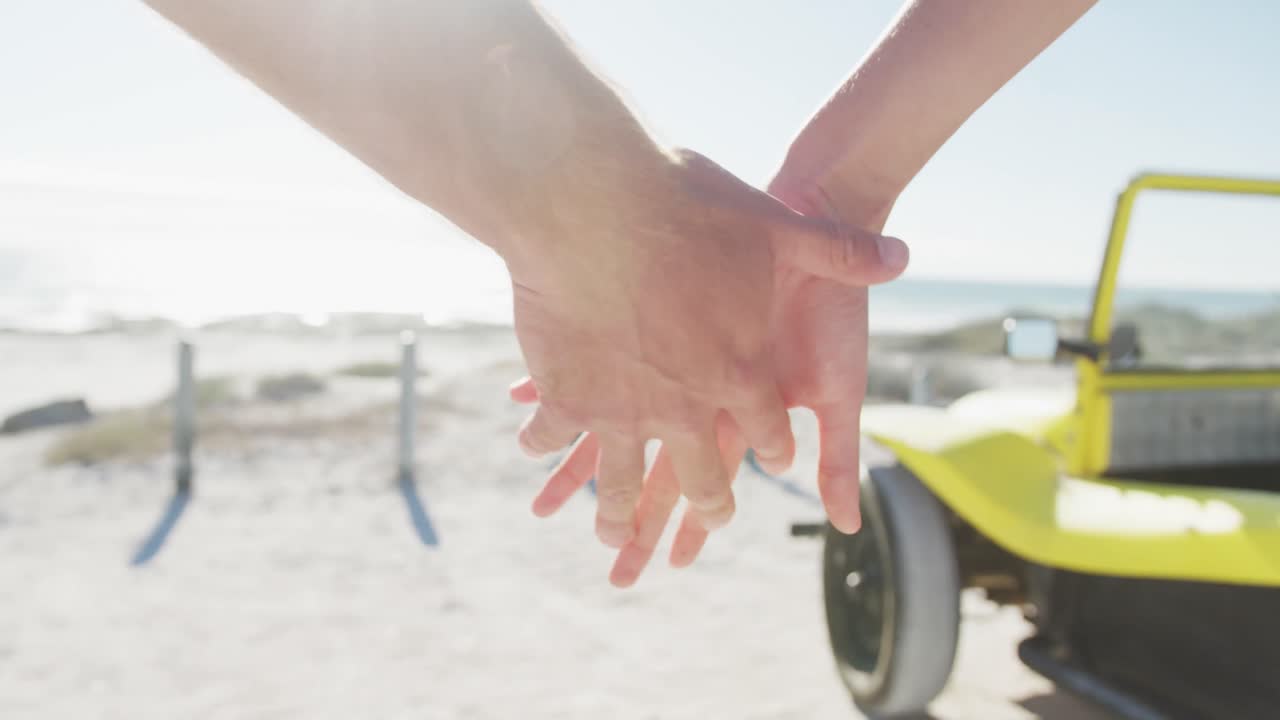 카우카시안 커플이 손을 잡고 바 ⁇ 가에 있는 해변 버기 근처에 서 있습니다.