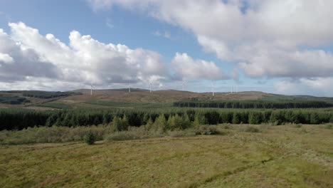 aerial drone footage slowly rising to reveal multiple turning wind turbines in a scottish windfarm surrounded by forestry plantations of commercial conifers on the kintyre peninsula, argyll, scotland