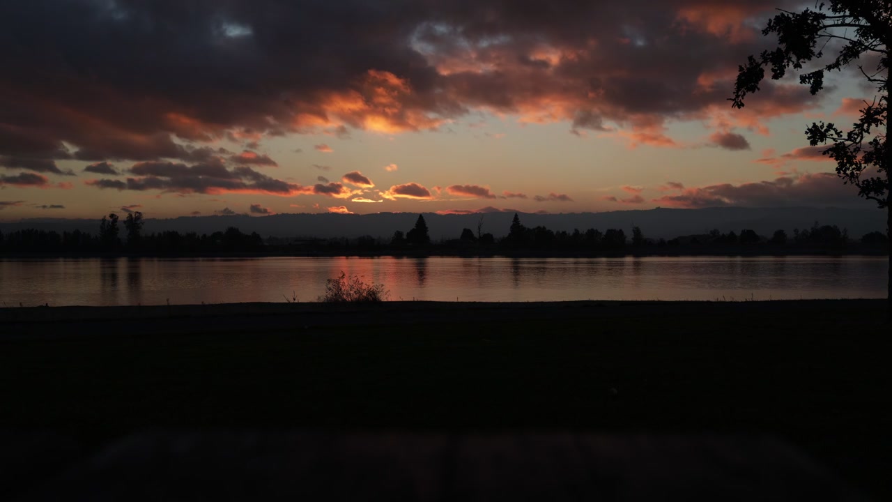 Ein Zeitraffer des Sonnenuntergangs am Columbia River fängt die Verwandlung des Himmels mit lebhaften Farbtönen ein, die sich auf dem Wasser spiegeln und die ruhige Schönheit des Flusses sowie das dynamische Abendlicht zeigen.