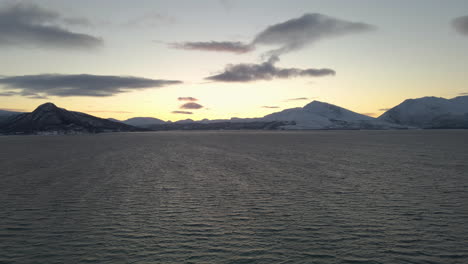 Vista-De-Pájaro-De-La-Puesta-De-Sol-Detrás-De-Montañas-Nevadas-Junto-Al-Mar-Noruego