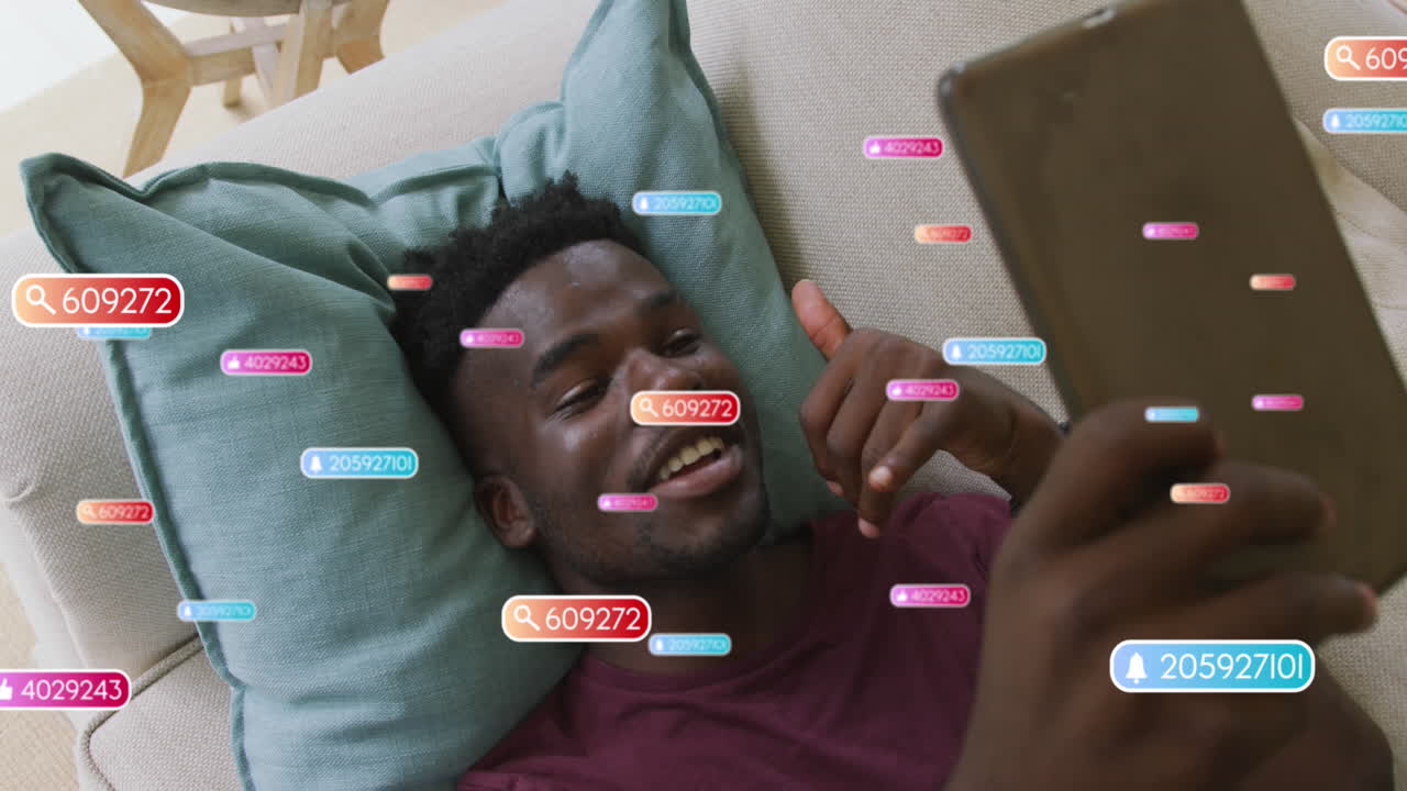 animación de iconos de redes sociales sobre un hombre afroamericano haciendo una llamada de video en una tableta en casa