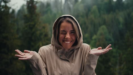 happy blonde girl rejoices in the forest rain in the mountains having fun and looking at the camera