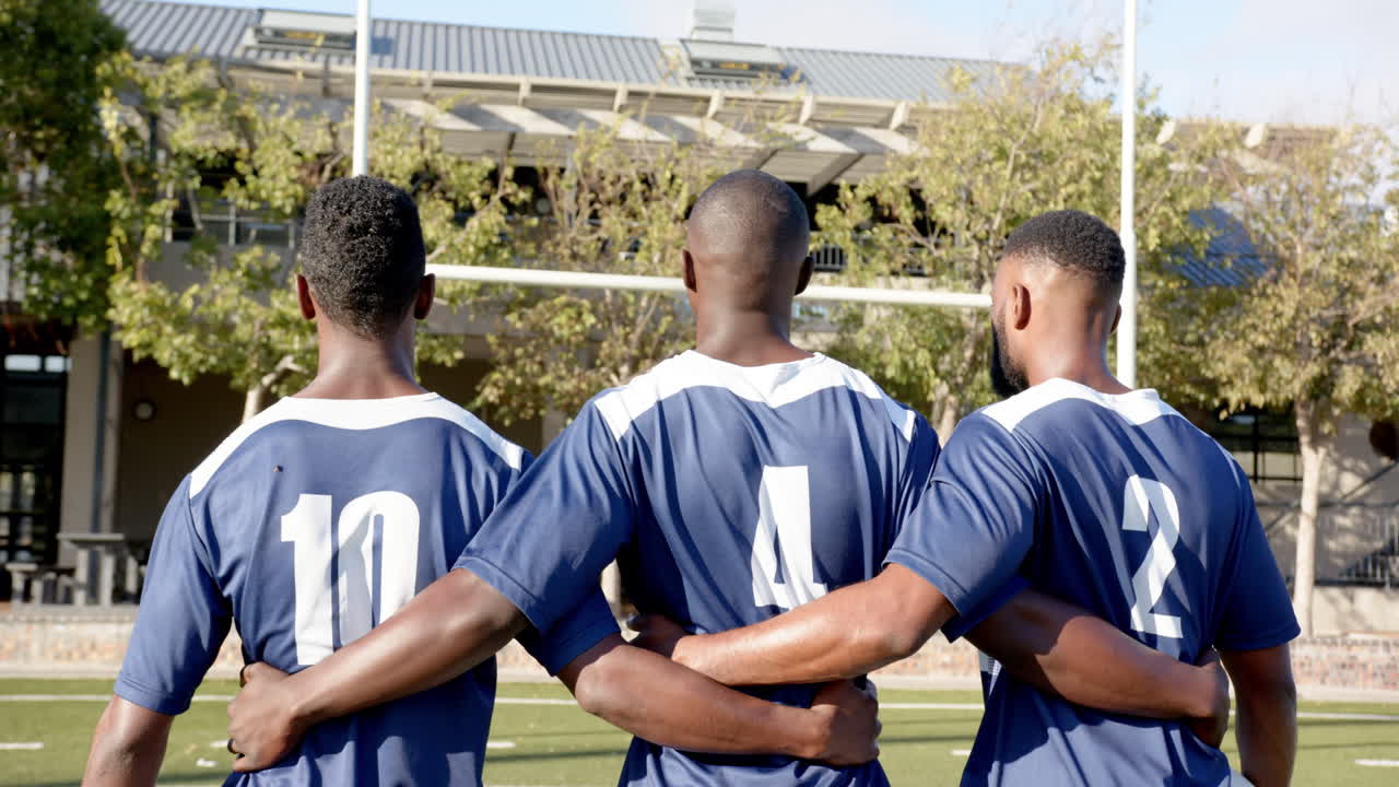 Football african american male players in blue jerseys standing on field, showing team unity