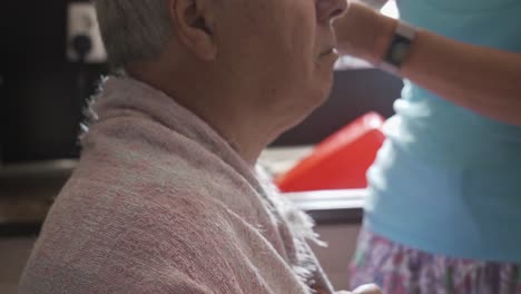 head profile of grey haired old man having haircut in home kitchen by amateur barber, left to right slide close up.