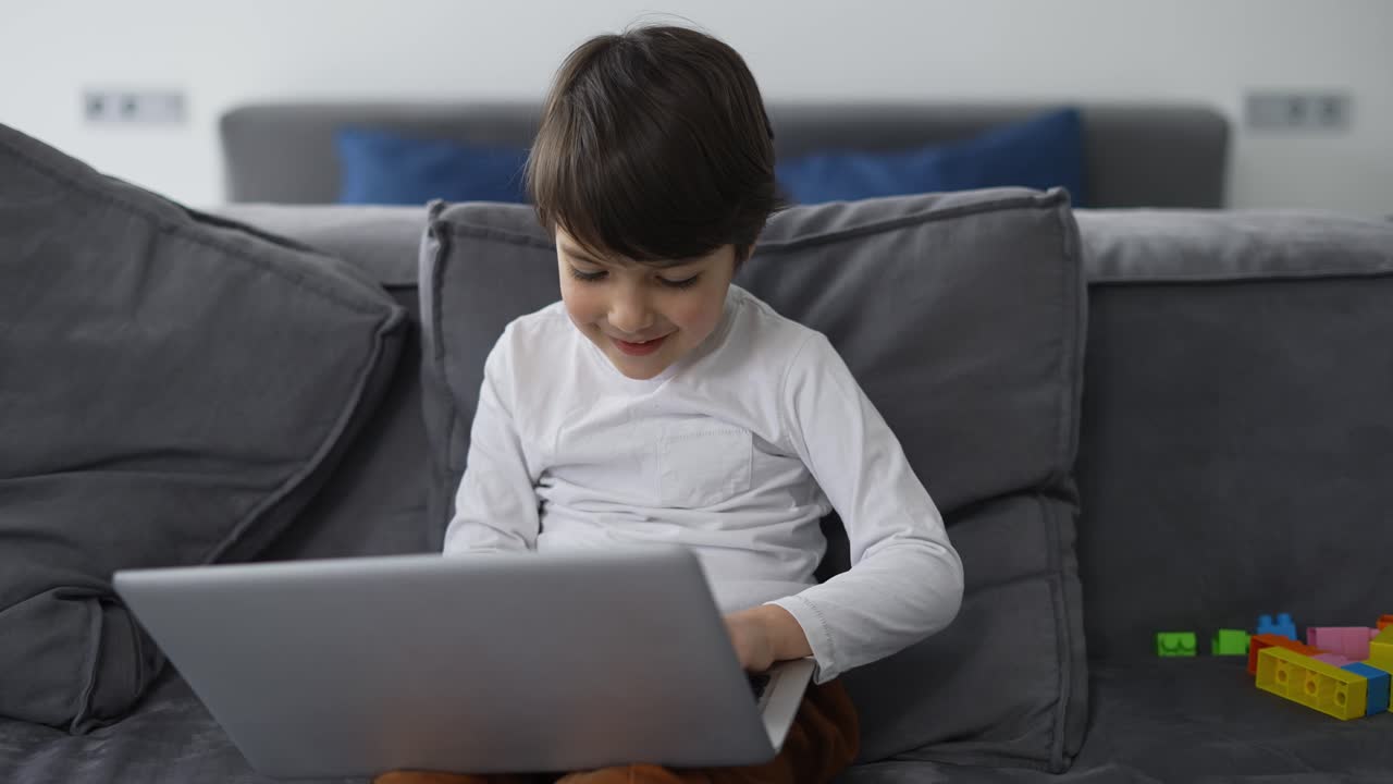 un niño lindo usa una computadora portátil sentado en el sofá solo