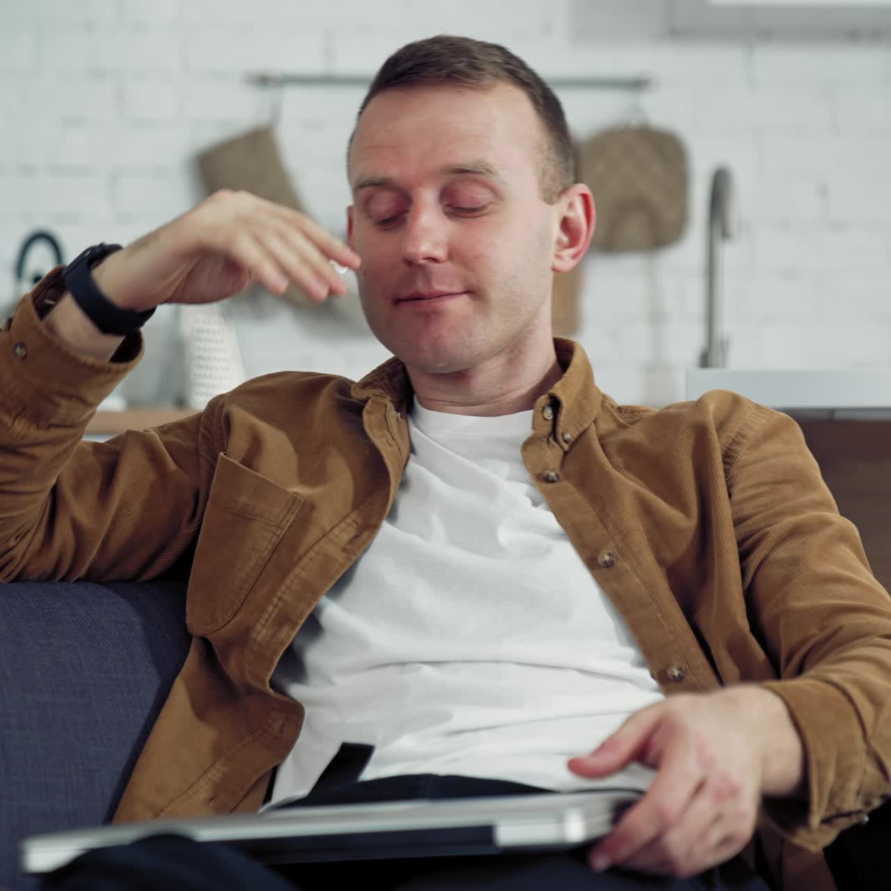 Young freelancer rests on sofa. Tired man puts his laptop off while sitting on the couch at home. Difficult remote job during coronavirus