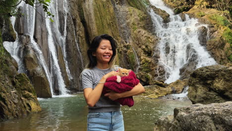 an asian girl carrying a cute cat in front of gò lào waterfall, mai châu, vietnam