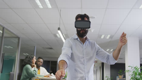 Happy-biracial-businessman-using-vr-headset-over-colleagues-in-office