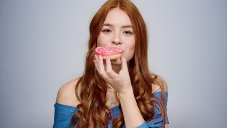 smiling woman eating doughnut indoors. excited girl having snack in studio