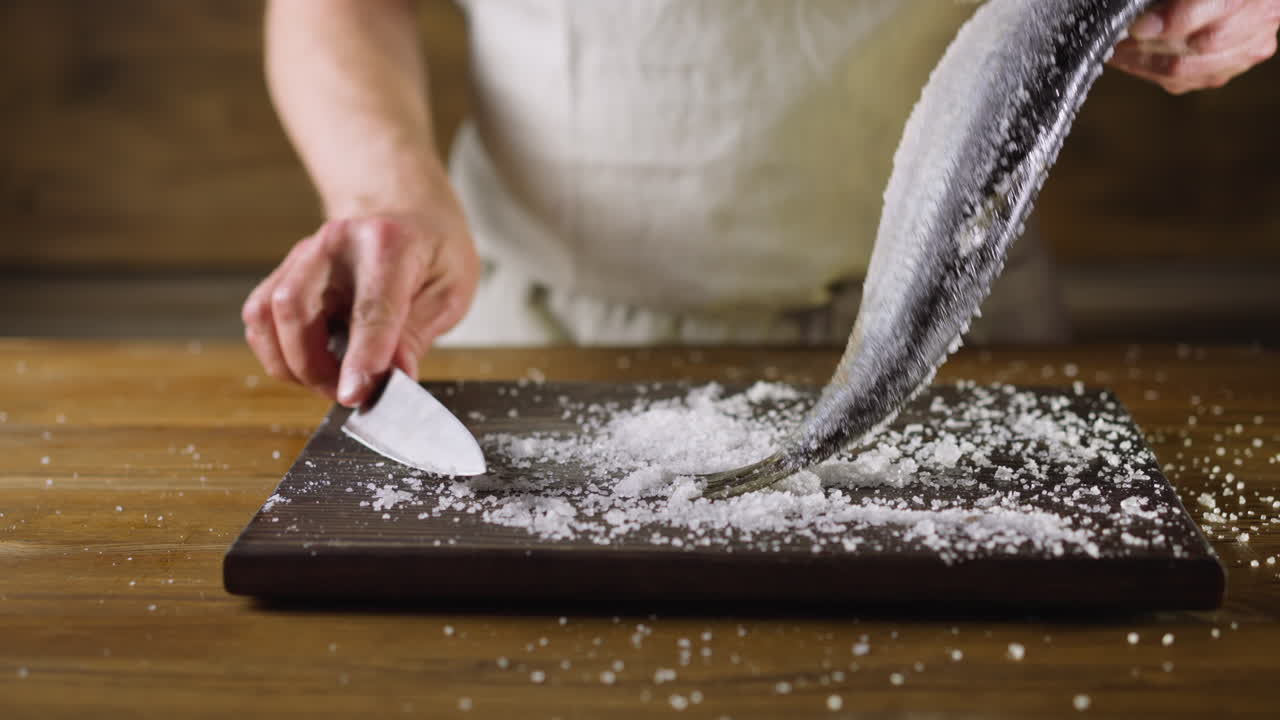 요리사는 절단판 위에 있는 헤링에서 소금을 흔들고