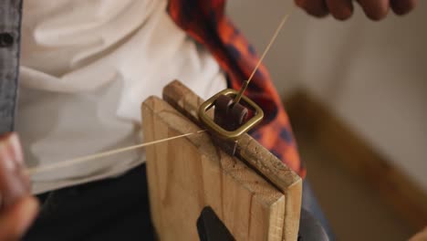 Hands-of-african-american-craftsman-preparing-belt-in-leather-workshop