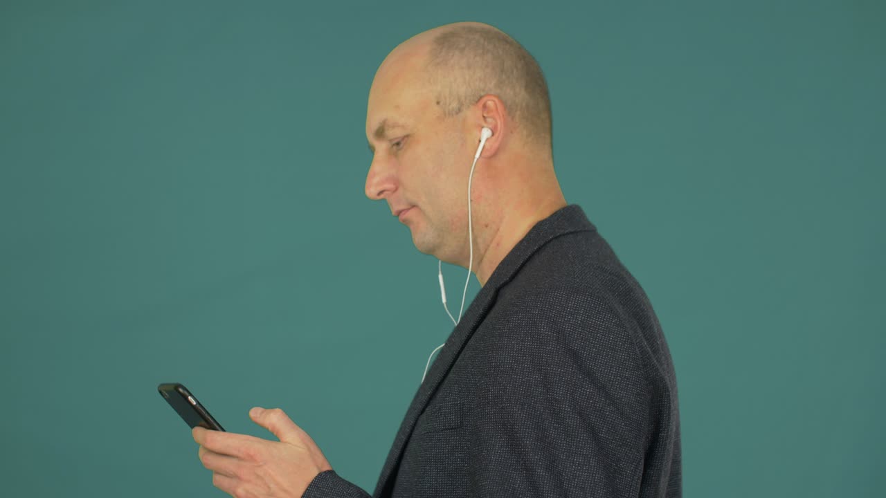 Bald middle aged businessman listening music with earphones and smartphone