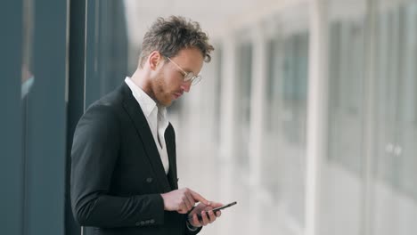 curly man in glasses with a phone in a glass corridor