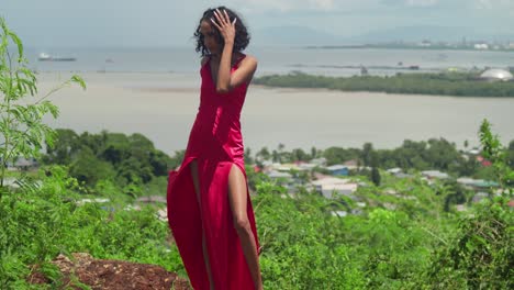 a young woman in a crimson dress looks out over the city from san fernando hill, with the coastline stretching out behind her