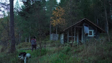hombre con su perro caminando a la vieja cabaña de madera en una mañana ventosa