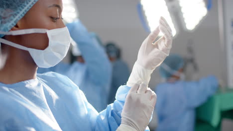 Portrait-of-african-american-female-surgeon-wearing-medical-gloves-in-operating-theatre,-slow-motion