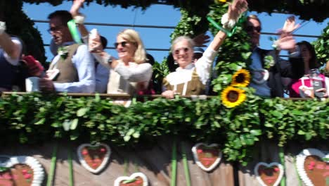 muscular horses pull a grand carriage, with joyful people waving to the cheering crowd along the street, spreading excitement throughout the oktoberfest area.
