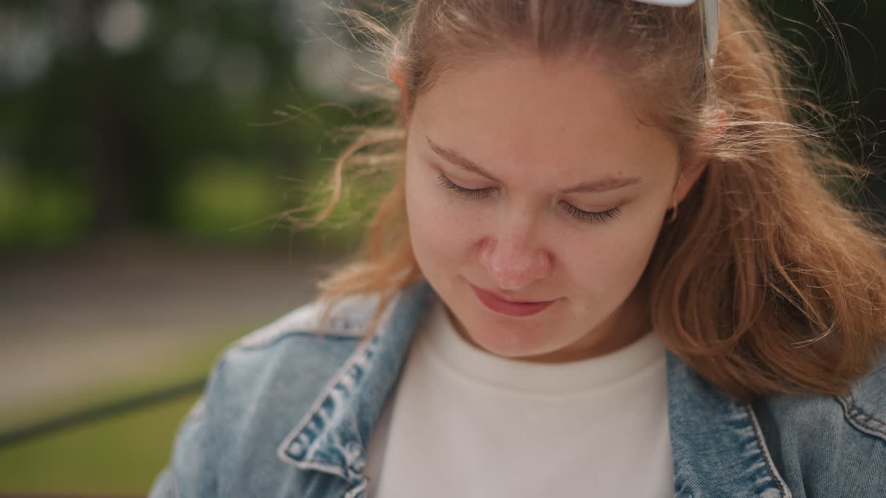 Silent reflective woman. Introspective woman gazing down thoughtfully. Contemplative woman in denim jacket with vape outdoors. Serene woman appears lost in thought on park bench during daylight