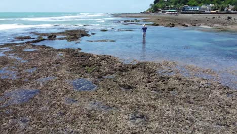 Fliegen-über-Gezeitenpools-Am-Strand-Mit-Kerl,-Der-Mit-Drohne-4k-In-Den-Ozean-Pipa-Beach,-Brasilien-Starrt