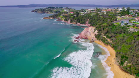cinematic drone shot flying backward over aslings rock pool in eden. starts with turquoise water, then reveals golden beach, dramatic cliffs, and town coastline