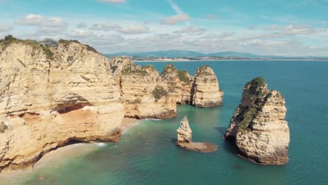 Weathered-limestone-rocks-rising-from-Algarve-mediterranean-sea,-in-Lagos,-Portugal---Aerial-fast-descending-fly-over-shot