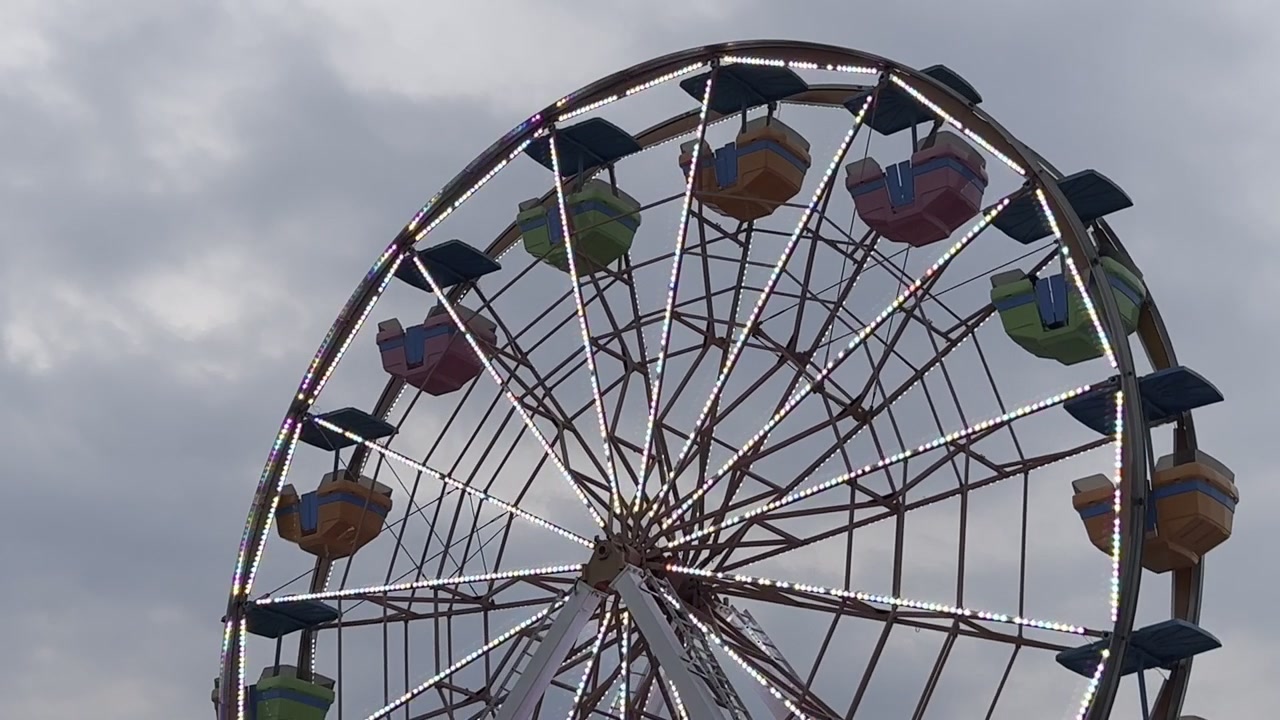 Ruota panoramica colorata gira contro un cielo nuvoloso, evocando un'atmosfera nostalgica da luna park.