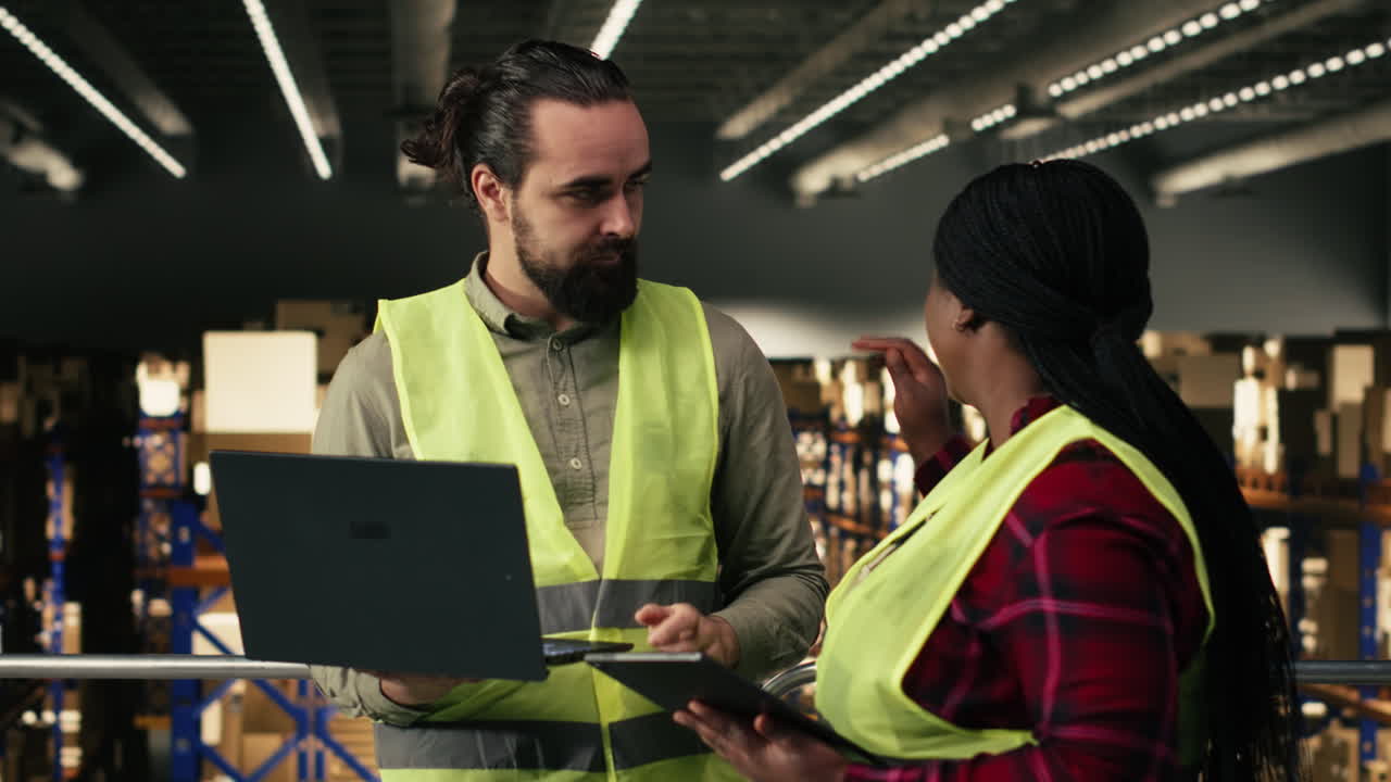 Diversi operai di magazzino che discutono l'inventario utilizzando un laptop e un tablet.