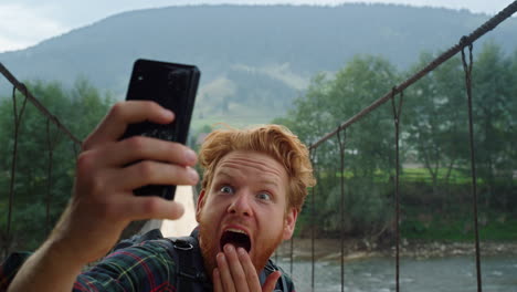 scared blogger taking selfie on river bridge. closeup traveler grimace on phone.