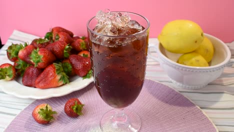 verter un vaso alto de té helado sobre un vibrante fondo rosa de verano con fresas y limones