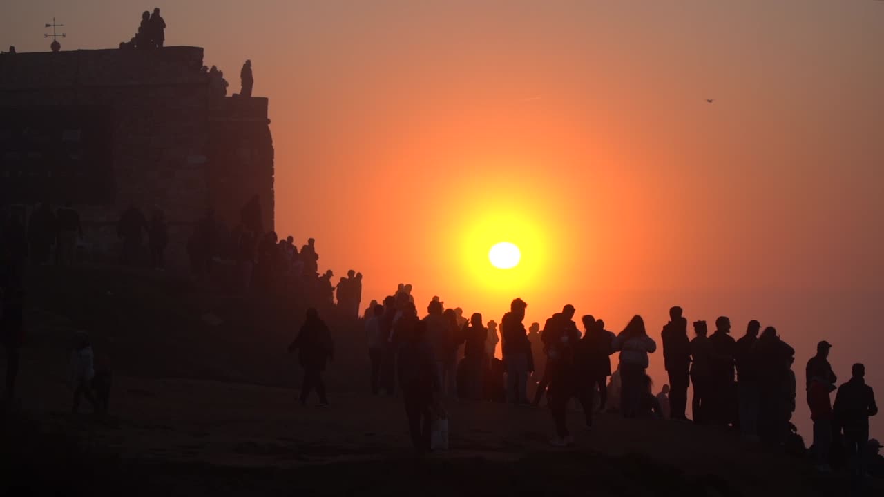 People Silhouette watching surfers riding giant waves in Nazare during Epic Sunset, Famous big waves in the World