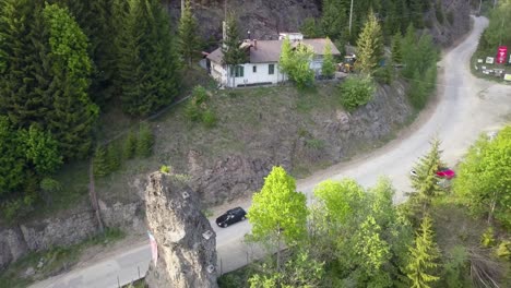 aerial pan of road next to green woodland with house in the foreground and cars