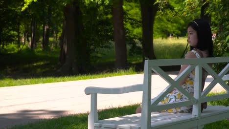 Lenta-Revelación-De-Una-Chica-Japonesa-Sentada-En-Un-Banco-Del-Parque-Con-Un-Vestido-De-Verano