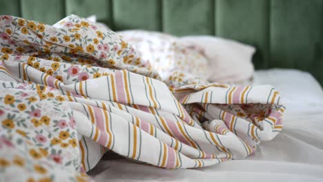 primer plano de una cama sin hacer con un cobertor floral y a rayas