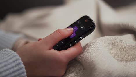 Close-up-of-remote-control,-woman-changing-channels-on-Roku-device-TV