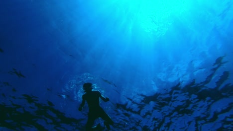 perspectiva submarina única de un tipo en forma nadando en los tonos oceánicos de azul con rayos de sol atravesando el agua