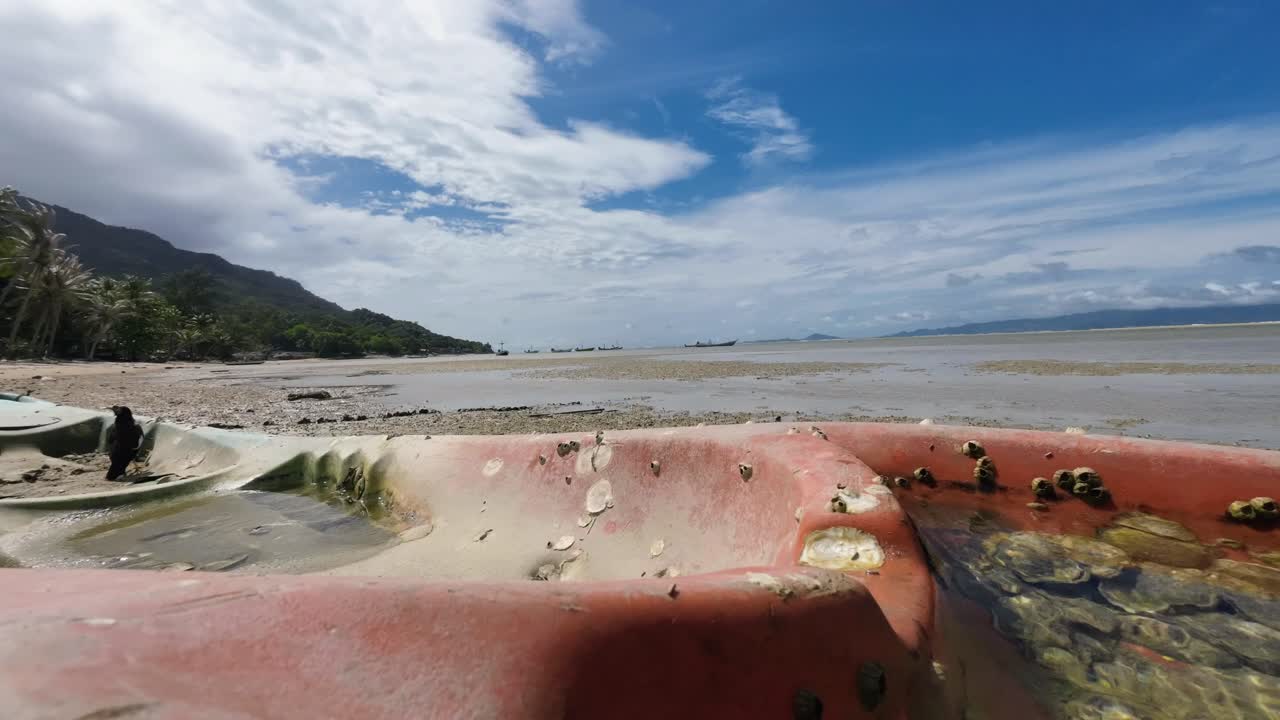 Timelapse footage of an old stranded kayak covered in seashells and algae on a sandy beach of Koh Phangan Thailand with moving clouds and scenic tropical seascape background