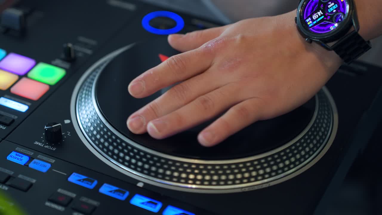Primo piano estremo della mano di un DJ professionista che fa scratch sul vinile su un piatto di giradischi digitale nero con jog wheel blu luminosa, pad di performance colorati e display della forma d'onda durante un set dal vivo