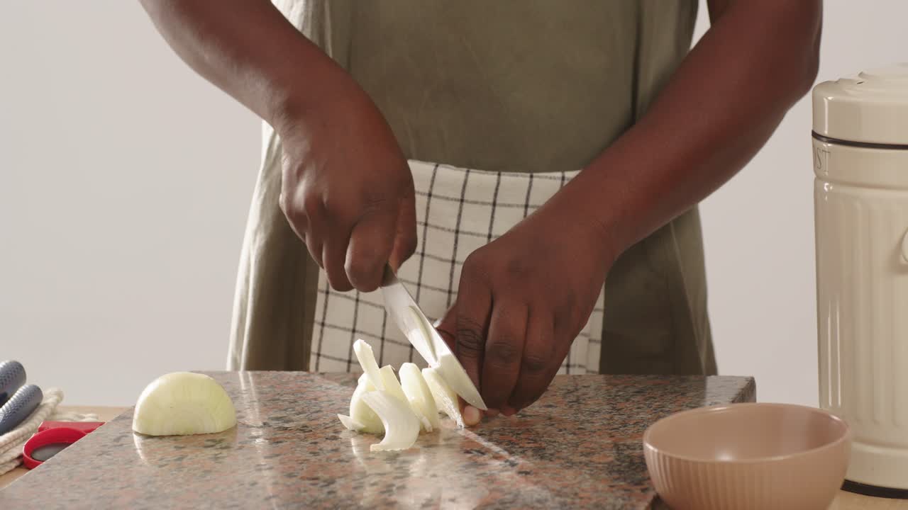 Midadult African American steadying halved onion on speckled counter slicing with knife for meal
