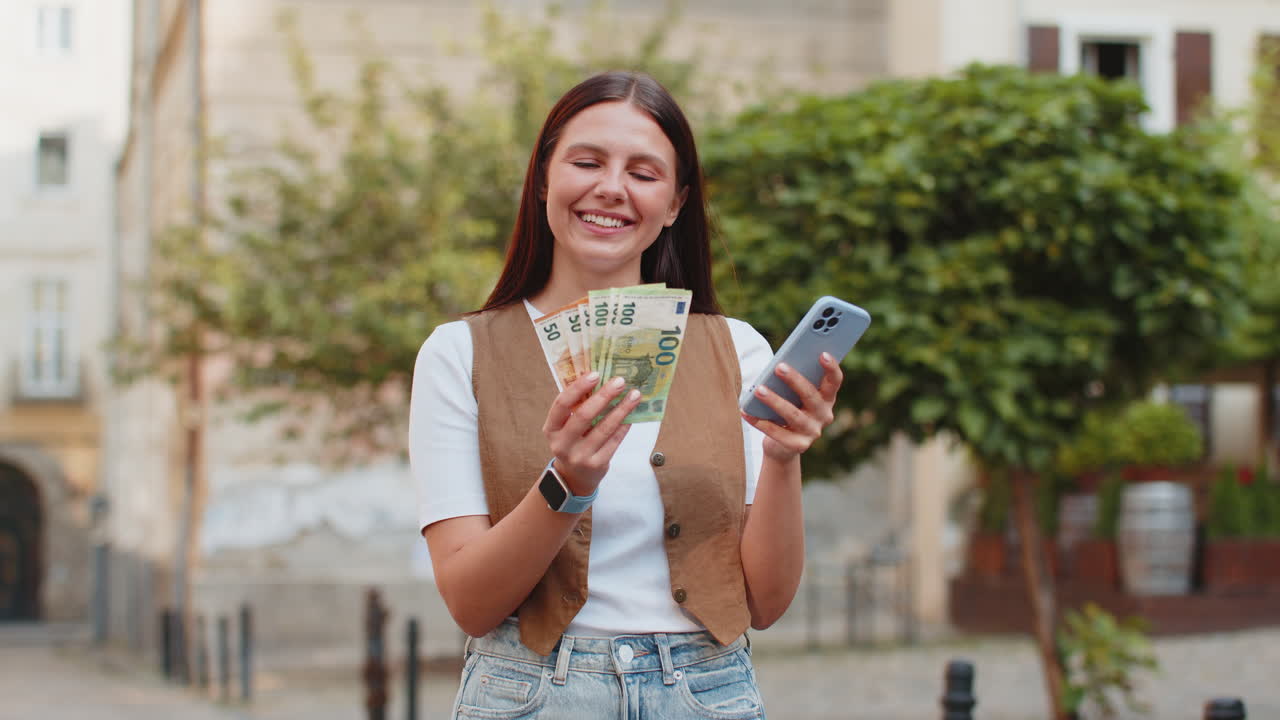Happy caucasian woman counting money euro cash using smartphone calculator app on city street