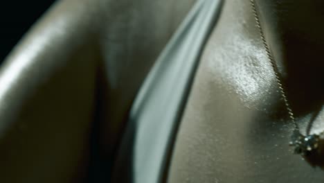 macro profile closeup of a woman’s sweaty collarbone, shoulder, and upper arm as she trains on a bike, with glistening skin highlighted by soft cinematic light in a dark, focused studio atmosphere