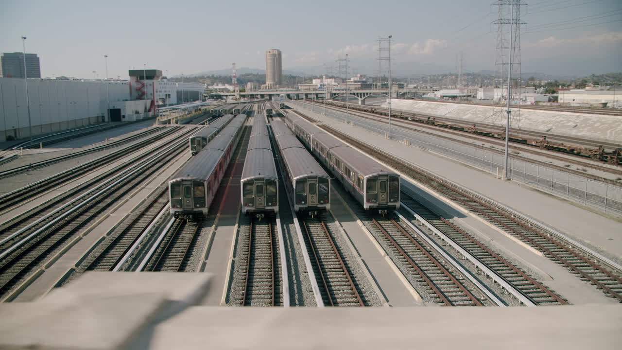 Trains parked in a large rail yard with power lines and city buildings in the background