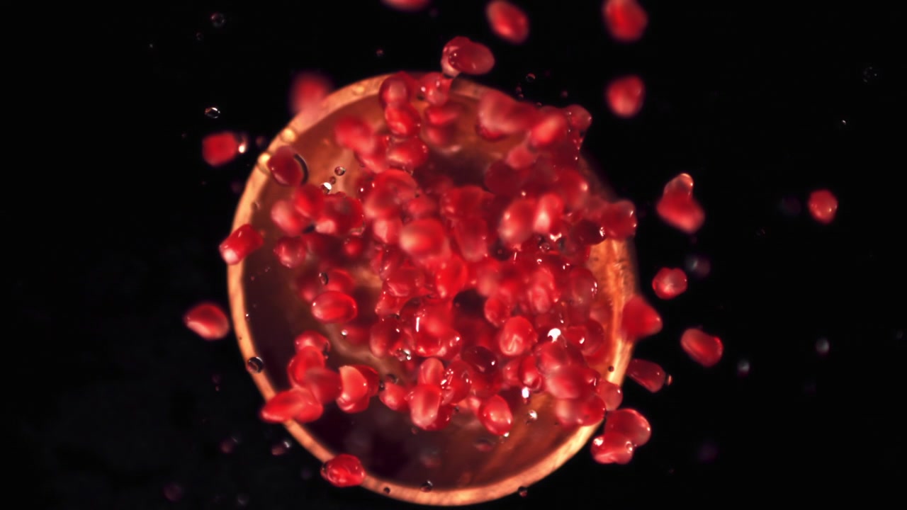 Røde granatæblekerner plasker i vand i slowmotion