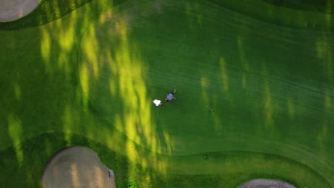 drone shot from above on the golf course during a sunny day with golfers putting the golf ball