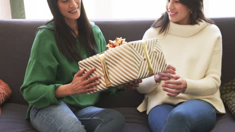 happy biracial mother and adult daughter exchanging christmas gift at home, slow motion