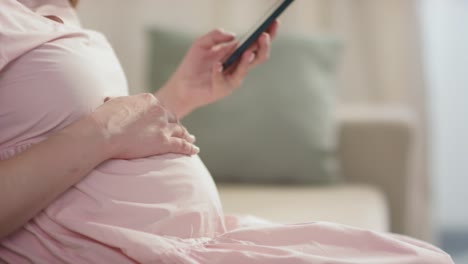 mujer embarazada con vestido rosa mirando el teléfono inteligente