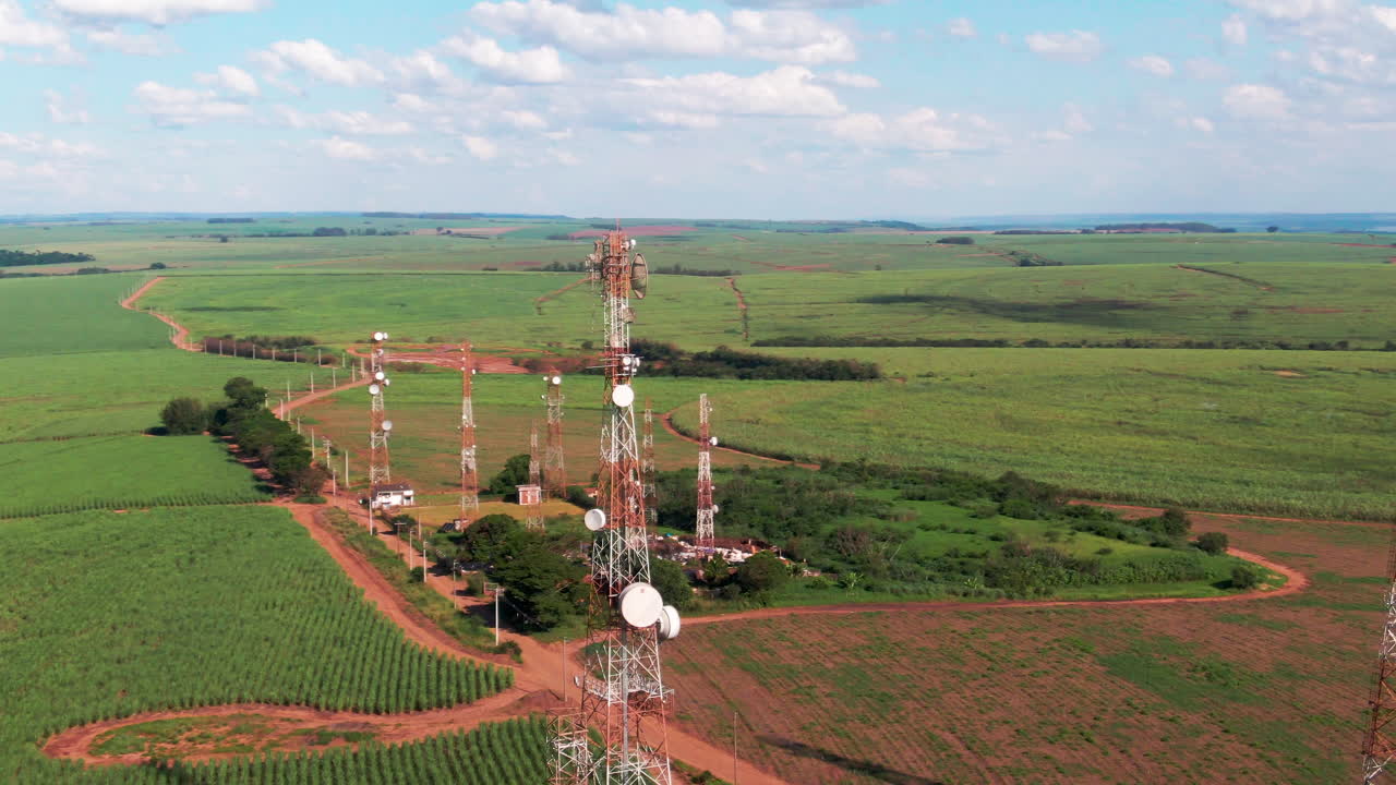 Pan drone view of telecommunication towers in rural areas of agriculture field during daytime.