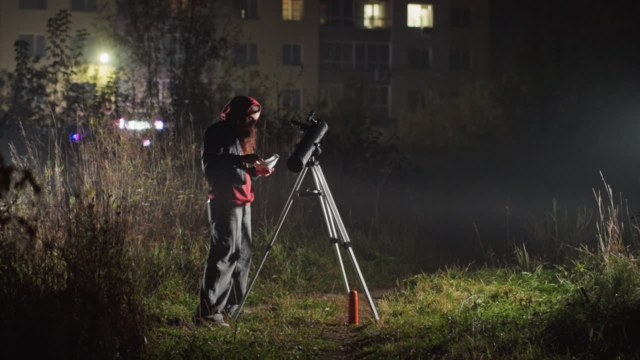 Mand justerer teleskop på byområde under svagt gadebelysning nær lejlighedsbygninger, tåge driver gennem højt græs, stativ skinner, fokuseret på stjerneundersøgelse, hobbyastronom kalibrerer montering