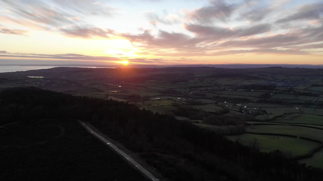Aerial view of Mutters Moor near Sidmouth, Devon, with the sun setting over the English Channel. Pull back shot